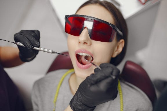 Woman laying in dental cahir with glasses on about to receive laser treatment