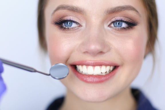 Woman smiling with dental mirror next to her teeth